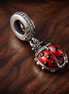 Red Ladybird Dangle Charm — display on walnut