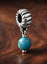 Turquoise-colored Dangle Charm — display on walnut
